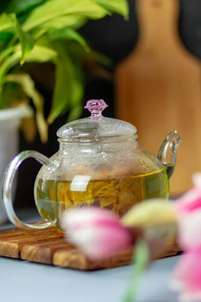 green tea with rose petals in a transparent teapot on a wooden table on a black background. The background is blurred. Tea drinking