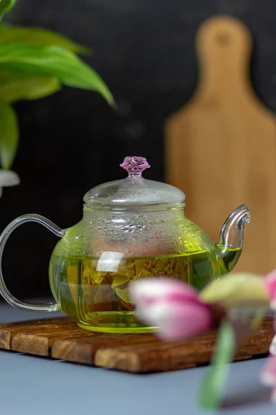 green tea with rose petals in a transparent teapot on a wooden table on a black background. The background is blurred. Tea drinking