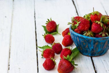 Olgun kırmızı çilekler ahşap beyaz bir masada mavi bir fincanda yatar. Tatlı böğürtlenler yakınlarda. Boşluğu kopyala