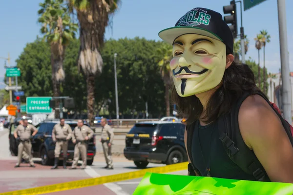 Anonymous with mascara with police in the background — Stock Photo, Image