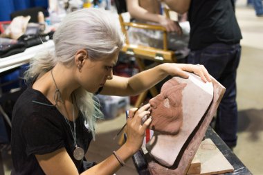 Young artist woman carefully sculpts details of horror mas