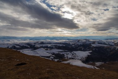 Batan güneş bulutlar aracılığıyla dağ sırasını aydınlatır. Bermamyt platosundan görüntü. Karachay-Cêess Cumhuriyeti, Rusya