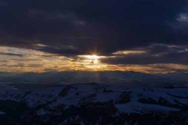 Batan güneş bulutlar aracılığıyla dağ sırasını aydınlatır. Bermamyt platosundan görüntü. Karachay-Cêess Cumhuriyeti, Rusya