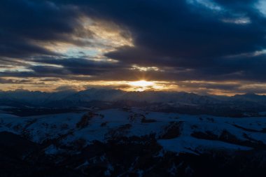 Batan güneş bulutlar aracılığıyla dağ sırasını aydınlatır. Bermamyt platosundan görüntü.