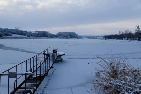 Gün batımında buzla kaplı bir gölün üzerindeki metal iskele.