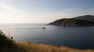 Bir katamaran ve küçük bir tekne adanın yanından geçiyor.