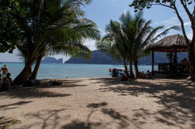 Tonsai sahilinde güneşli bir öğleden sonra insanlar palmiye ağaçlarının gölgesinde dinlenir.