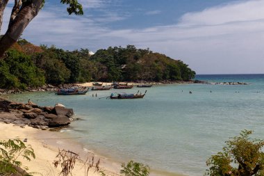 Kayalar ve kumlu bir sahil. Körfezde birkaç tekne var. Peo