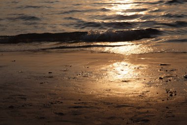 Batan güneş kumlu sahildeki deniz dalgalarına yansıyor.