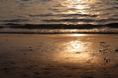 Batan güneş kumlu sahildeki deniz dalgalarına yansıyor.