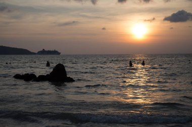 İnsanlar akşam denizinde bir kayanın arka planında yıkanırlar.