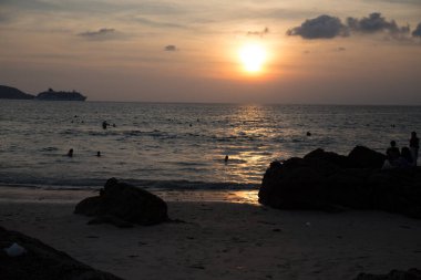 İnsanlar akşam denizinde bir kayanın arka planında yıkanırlar.