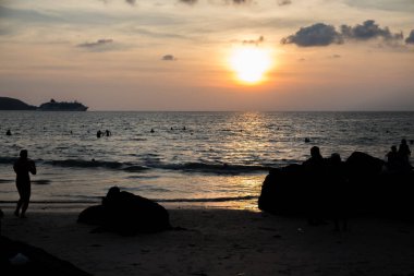 İnsanlar akşam denizinde bir kayanın arka planında yıkanırlar.