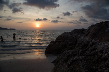 İnsanlar akşam denizinde bir kayanın arka planında yıkanırlar.
