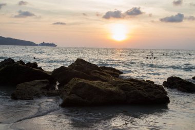 İnsanlar akşam denizinde bir kayanın arka planında yıkanırlar.