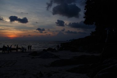 Sahilde gün batımından sonra insanların siluetleri.