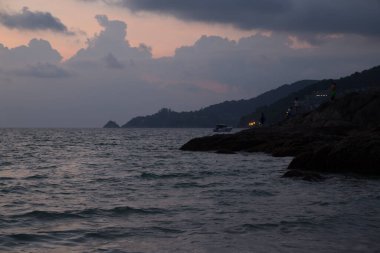 Kıyıdaki kayalıklarda insanlar gün batımını izliyor.
