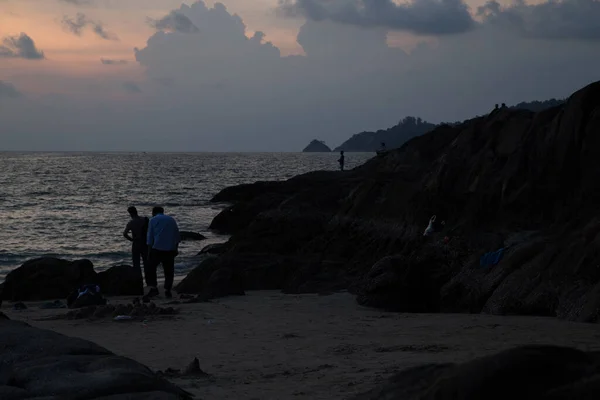 Sahilde gün batımından sonra insanların siluetleri.