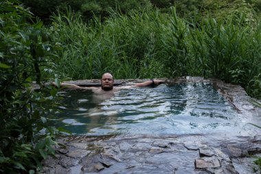 Bir adam ormanın ortasında kaynak suyuyla yazı tipi içinde dinleniyor. Zmeika Dağı, Stavropol Bölgesi, Rusya