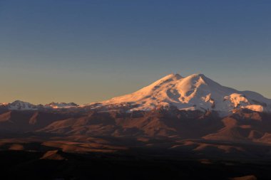 Elbrus bulutsuz bir sabahta güneşin doğuşunun pembe ışınlarında. Manzara Bermamyt platosundan, Karachay-Cêess Cumhuriyeti, Rusya