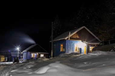 Dağlardaki köyün kış manzarası. Bir sürü taze kar. Cipler evlerin yakınına park edilmiş. Sokak ışıkları parlıyor.