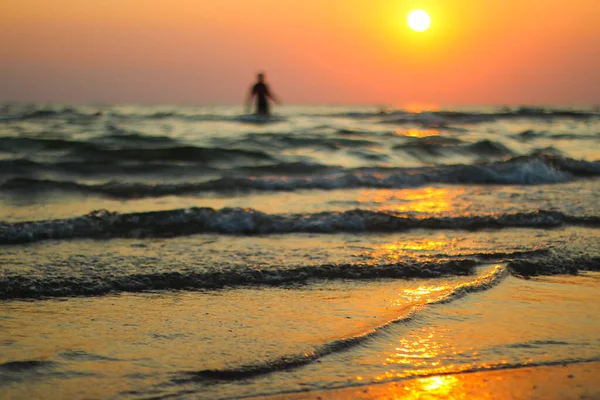 O homem relaxado está andando sobre as ondas. Areia molhada dourada na praia em um fundo de pôr do sol. — Fotografia de Stock