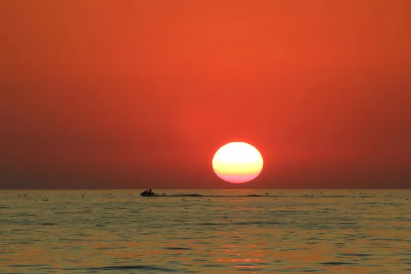 Человек наслаждается жизнью, катаясь на водном мотоцикле на фоне заката моря — стоковое фото