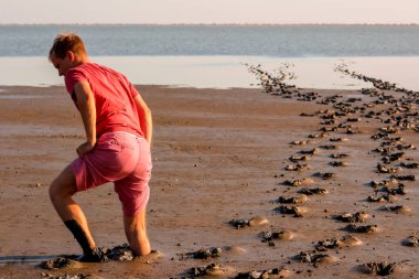 Kırmızı tişörtlü ve pembe şortlu Avrupalı yalın ayak genç adam çamura daldı.