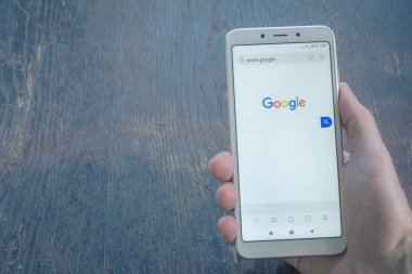 St. Petersburg, Rusya, 22 Temmuz 2019. Beyaz akıllı telefon ahşap masa arkasında. Cep telefonu ekranında Google web sitesi