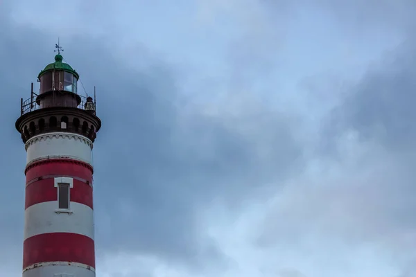 Fırtınalı bir gökyüzünün arka planında kırmızı ve beyaz çizgili deniz feneri. Tasarım veya metin için boş kopyalama alanı