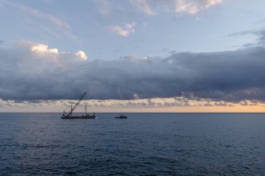 İtalya 'nın Liguria kıyısındaki kara ıslah çalışmaları sırasında römorkör sahil şeridinin yanında bir vinç mavnası çekiyor.