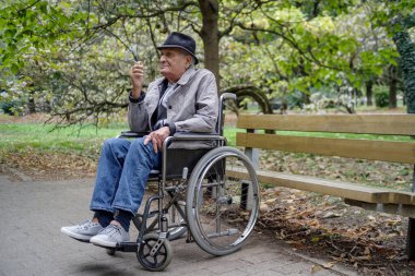 Tekerlekli sandalyede sigara içen yaşlı bir adam.