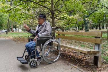 Tekerlekli sandalyede sigara içen yaşlı bir adam.