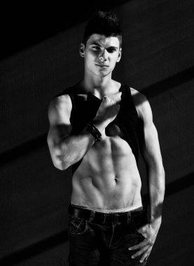 Yakışıklı genç bir adam tişörtünü alır ve gövdesini gösterir.