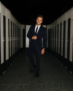 Spor salonunun soyunma odasında siyah takım elbiseli, gülümseyen adam.