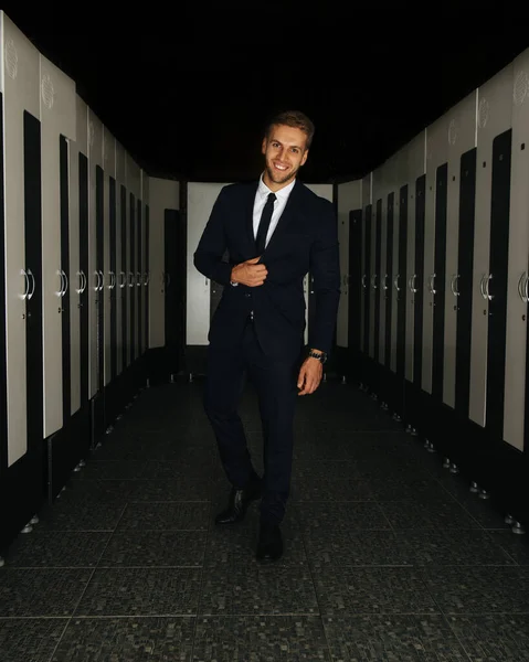 Spor salonunun soyunma odasında siyah takım elbiseli, gülümseyen adam.