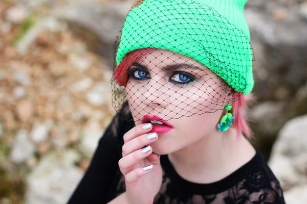 Ritratto di una bella adolescente con gli occhi azzurri in un cappello di colore verde alla moda ed elegante con velo nero seduto sul mare sulle rocce giallo — Foto Stock