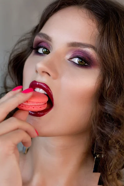 Belle et charmante brune dans un style sicilien aux yeux verts avec des couleurs de maquillage Marsala. Une fille tenant un délicieux gâteau et mangeant des macaronis — Photo