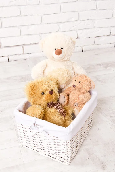 Stuffed teddy bears in a basket on the floor. A white wainscot. — Stock Photo, Image