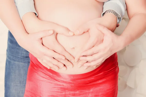 Padres manos haciendo un corazón en el vientre de la madre embarazada — Foto de Stock