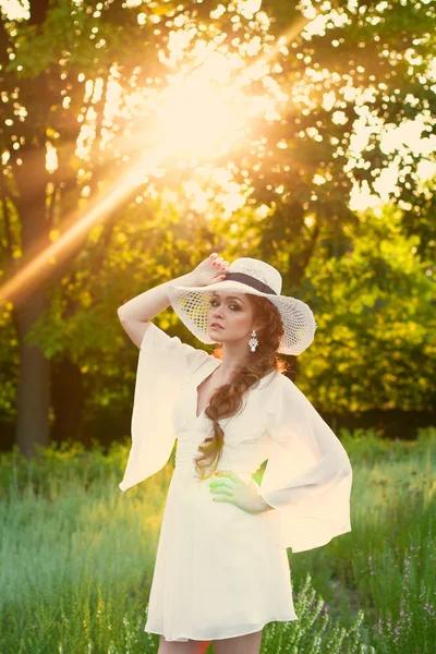 Bella ragazza dai capelli rossi in un elegante cappello di paglia in un giardino botanico — Foto Stock