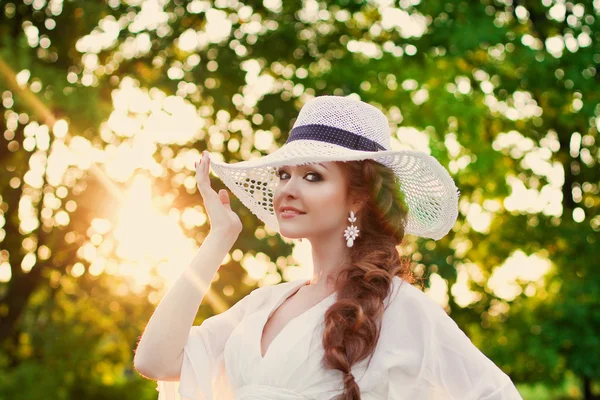 Bella ragazza dai capelli rossi in un elegante cappello di paglia in un giardino botanico — Foto Stock