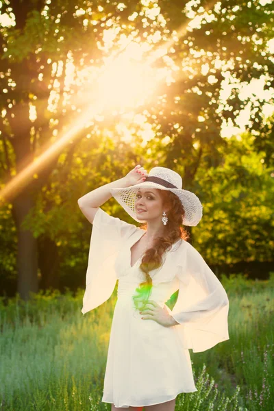 Mooie roodharige meisje in een stijlvolle stro hoed in een botanische tuin — Stockfoto