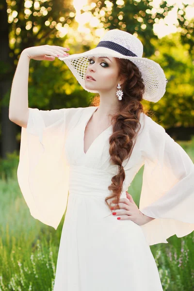 Красивая рыжая девушка в стильной соломенной шляпе в ботаническом саду — стоковое фото