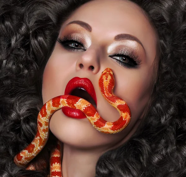 Gros plan portrait de femme sexy avec des lèvres rouges, les cheveux longs et beau maquillage, tenant dans sa bouche le serpent exotique — Photo