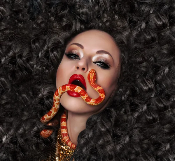 Ritratto ravvicinato di donna sexy con labbra rosse, capelli lunghi e bel trucco, tenendo in bocca il serpente esotico — Foto Stock