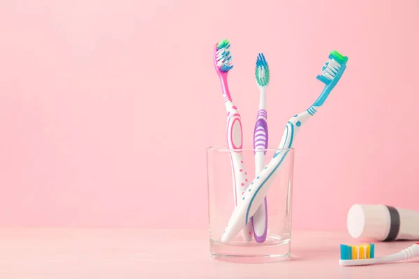 Toothbrushes in glass with tube of toothpaste on pink background. Top view