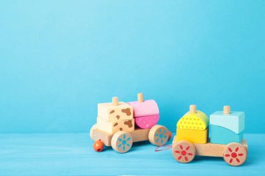 Mavi arka planda, gölge yansıması olan küçük çocuklar için tren oyuncağı istiflemek. Tahta geometrik bloklardan yapılmış bebek treni. Çocuklar için renkli ahşap istifleme treni