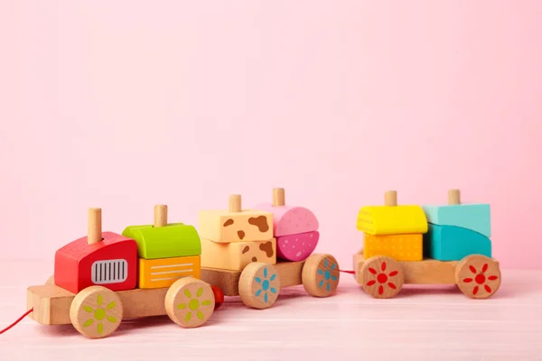 Stacking train toddler toy for little children on pink background with shadow reflection. Baby train made of wooden geometric blocks. Colorful wooden stacking train for kids