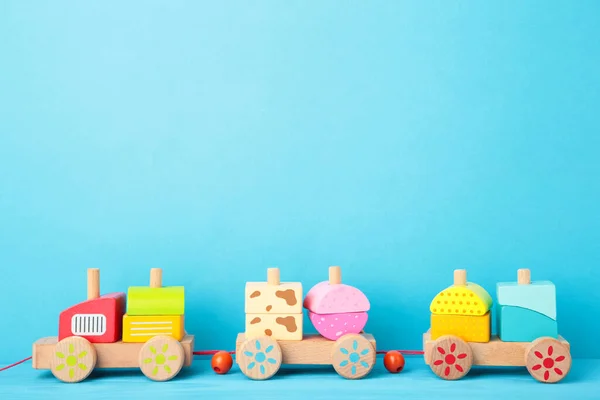 Stacking train toddler toy for little children on blue background with shadow reflection. Baby train made of wooden geometric blocks. Colorful wooden stacking train for kids